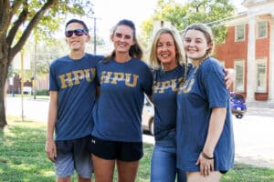 Four individuals wearing matching "Howard Payne University Hawks" t-shirts posing together outdoors. | HPU