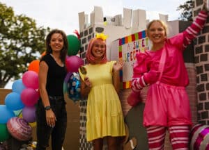 Three individuals in Howard Payne University festive attire with balloons celebrating at an outdoor event. | HPU
