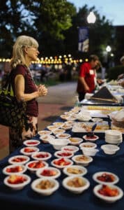 Woman standing beside a table lined with desserts at a Howard Payne University outdoor event in the evening. | HPU