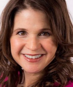 A close-up portrait of a smiling woman with brown hair wearing a Howard Payne University pink top. | HPU