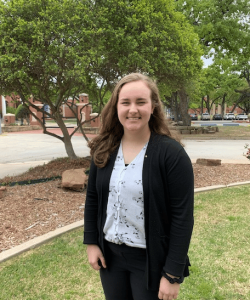 A smiling woman standing outdoors in Howard Payne University's campus in casual business attire. | HPU